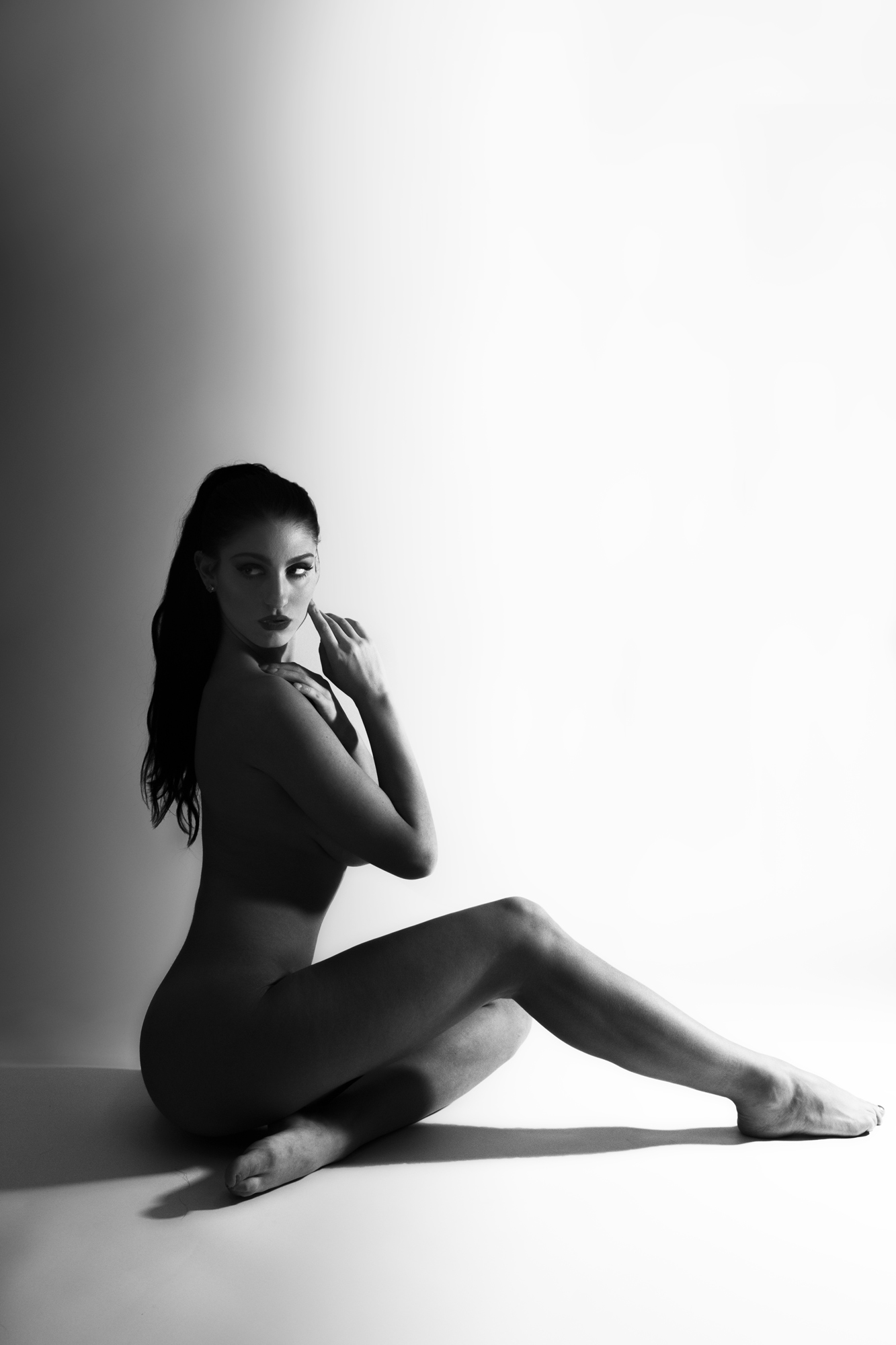 A woman sits on the floor with her legs extended, looking at the camera, in a black and white photo.