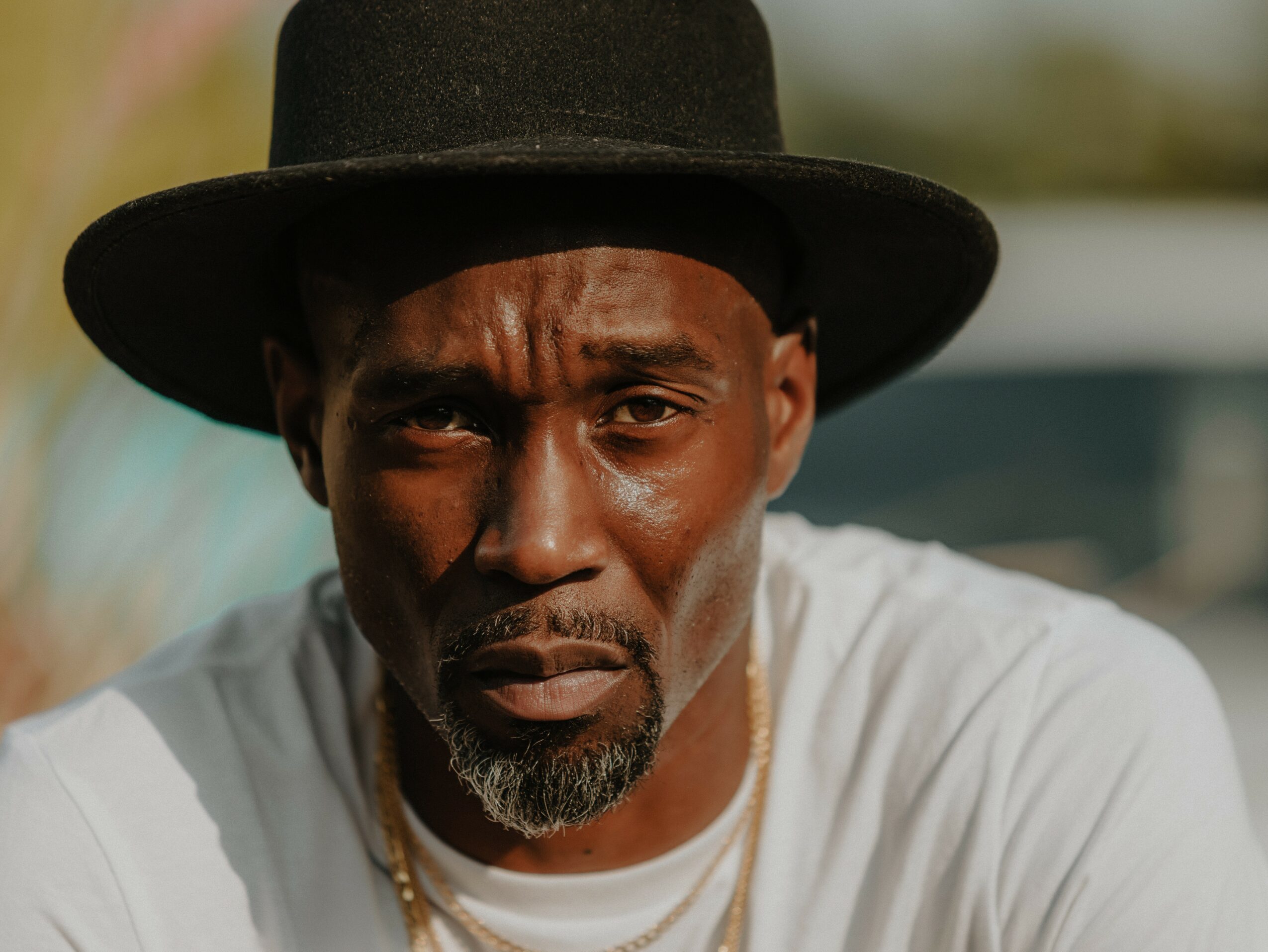 Man wearing a black hat and white shirt, looking directly at the camera with a serious expression.