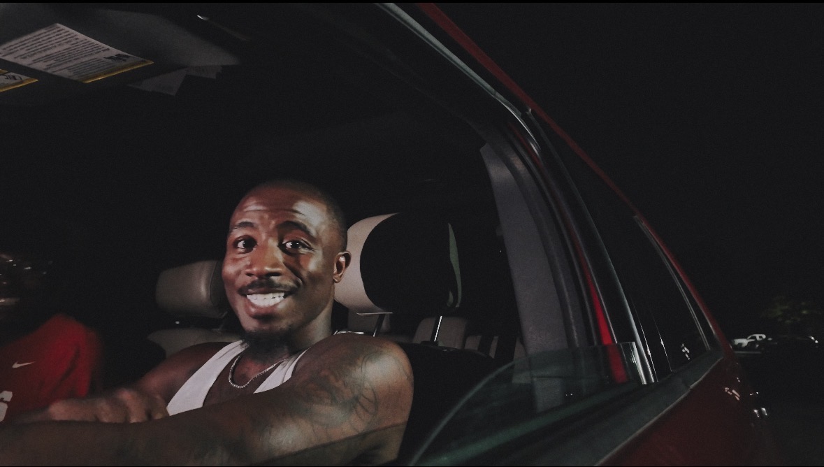 Person smiling inside a car at night, with a dark background and visible car interior.