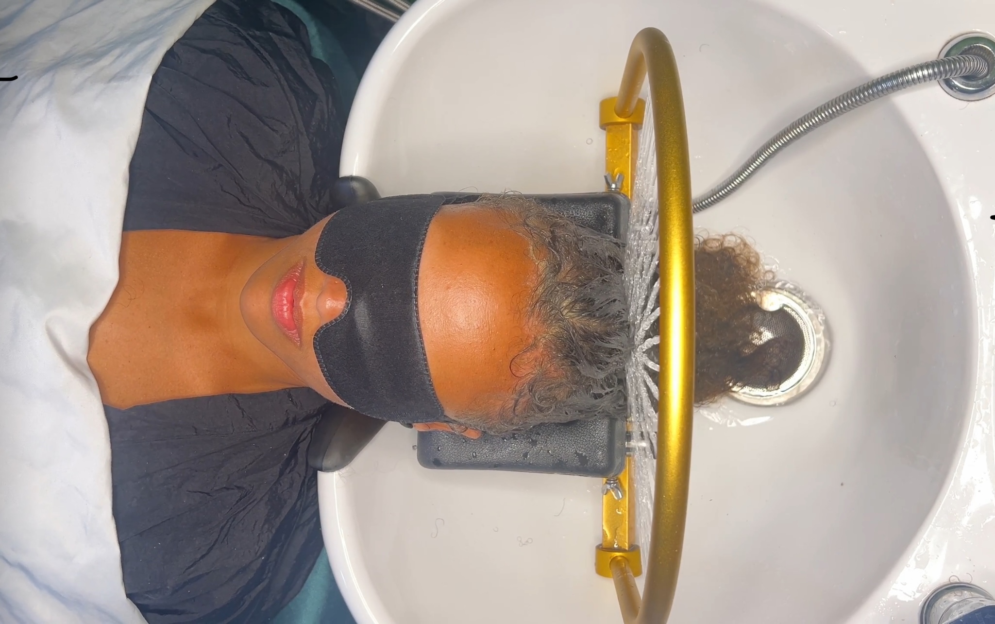 Person with head under a shower head in a white bathtub, water running, hair wet, wearing a black shirt.
