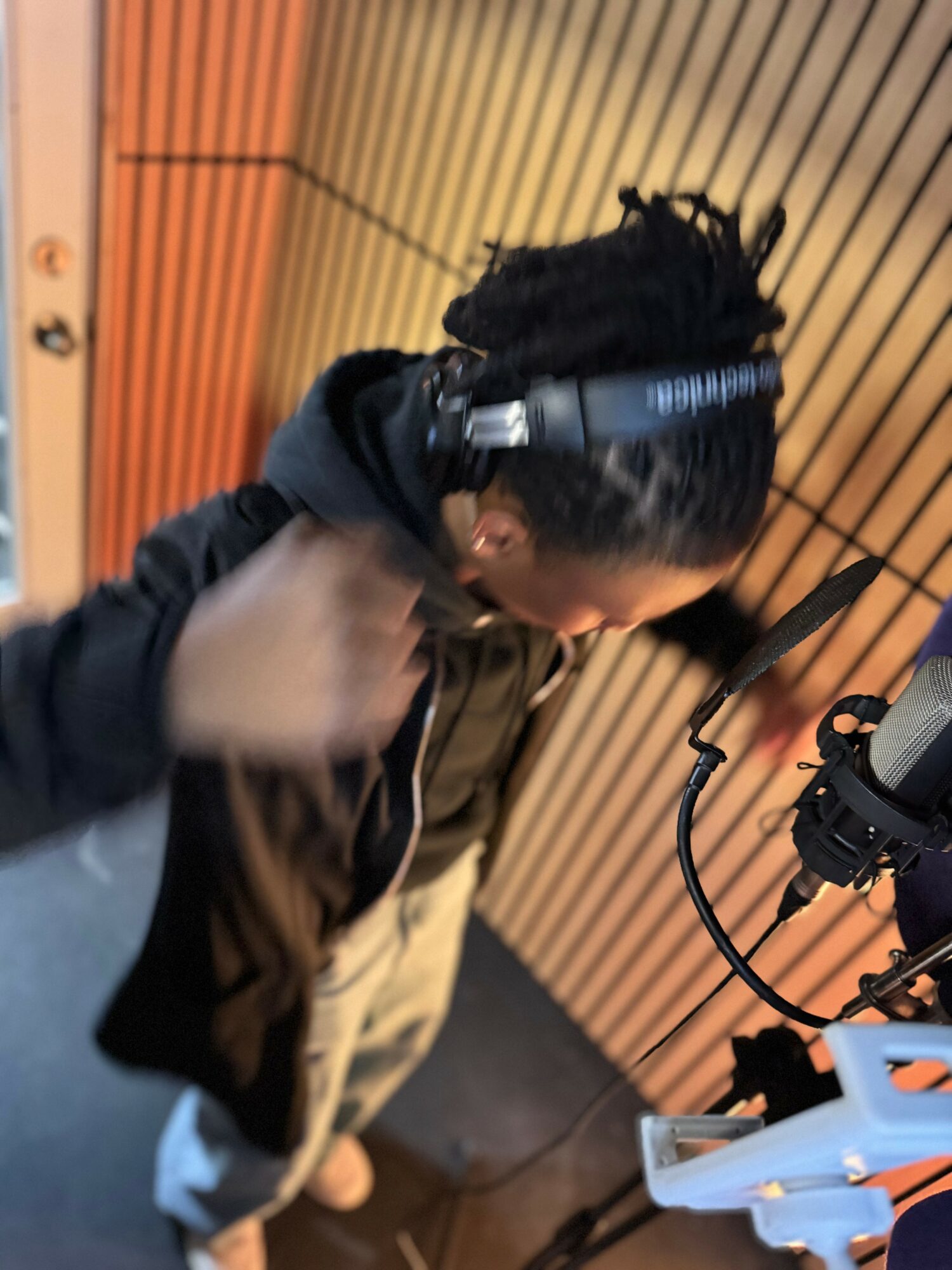 Person with dreadlocks adjusting headphones in a recording studio with wooden panel walls.