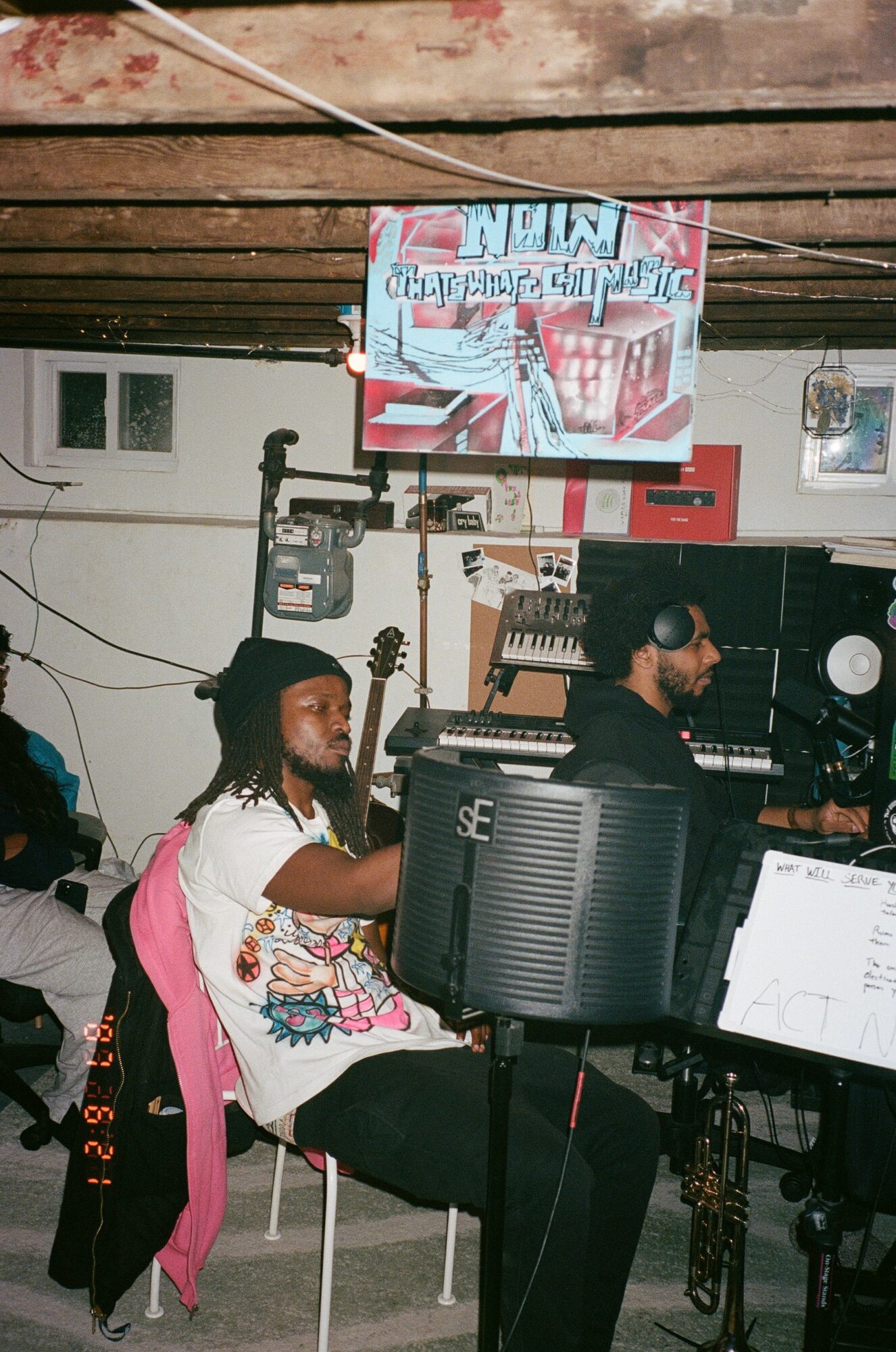 Two people working at a music production setup in a room with exposed wooden ceiling beams and various equipment.