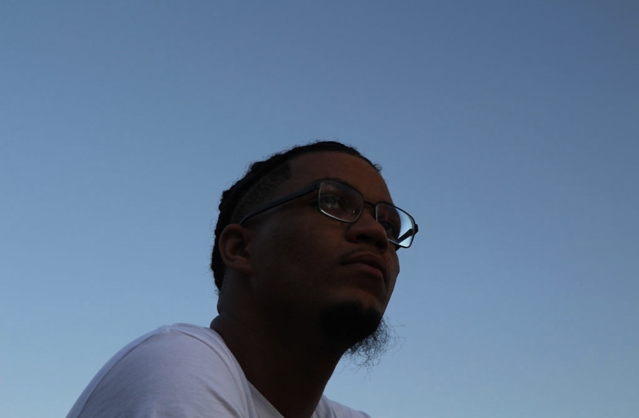Young person with glasses looking to the side against a clear sky, low light, and shadowed face.