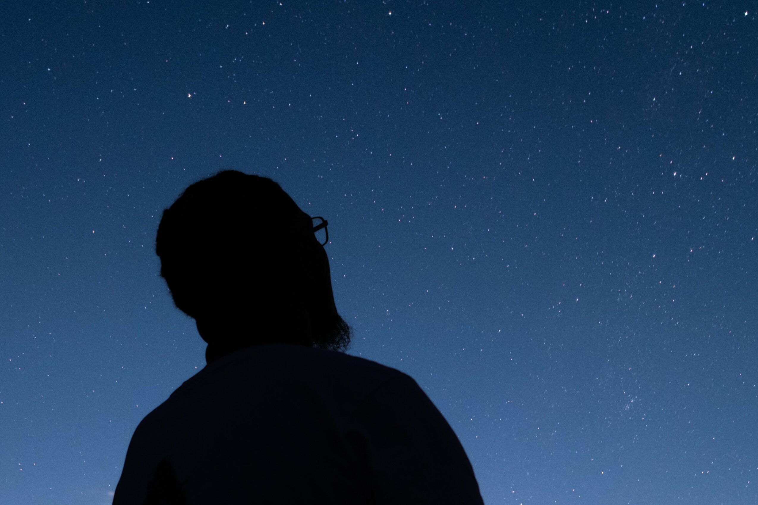 Silhouette of a person with glasses looking at a starry night sky.