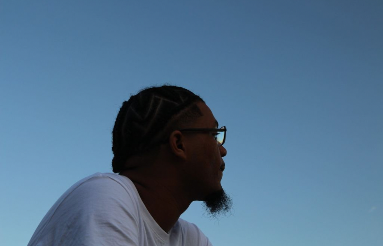 Profile of a person with braided hair and glasses against a clear blue sky.