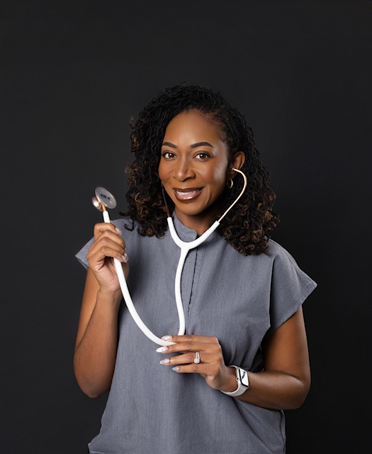 Woman with curly hair wearing a gray top, holding a stethoscope, smiling, against a dark background.