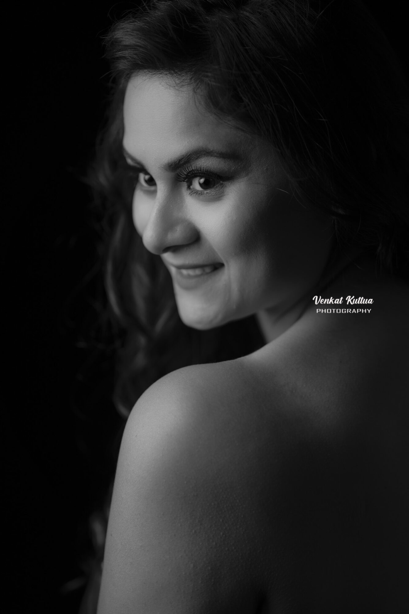Portrait of a smiling woman with dark hair, looking over her shoulder, in black and white.