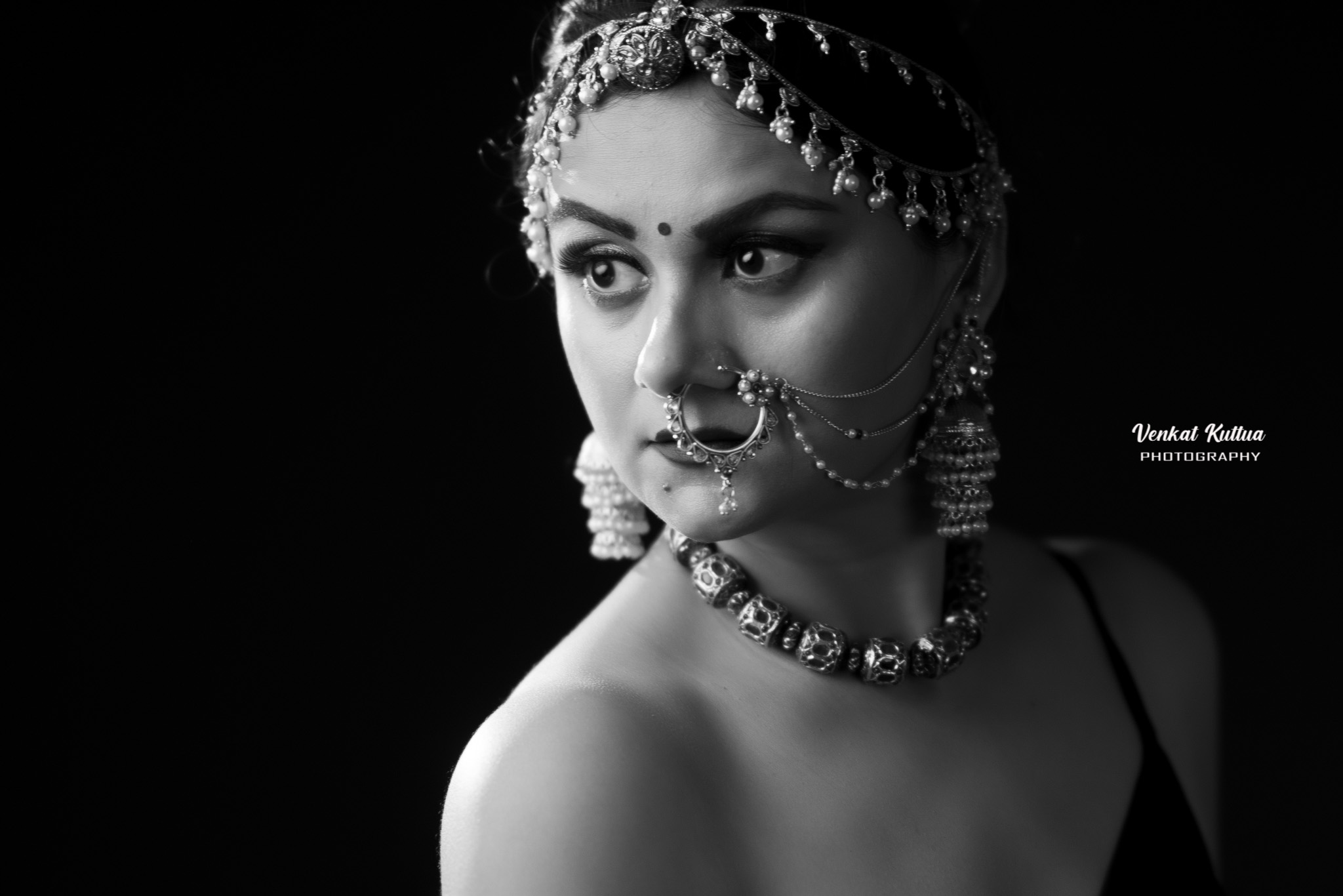 Black and white portrait of a woman wearing traditional jewelry, looking to the side with a serious expression.