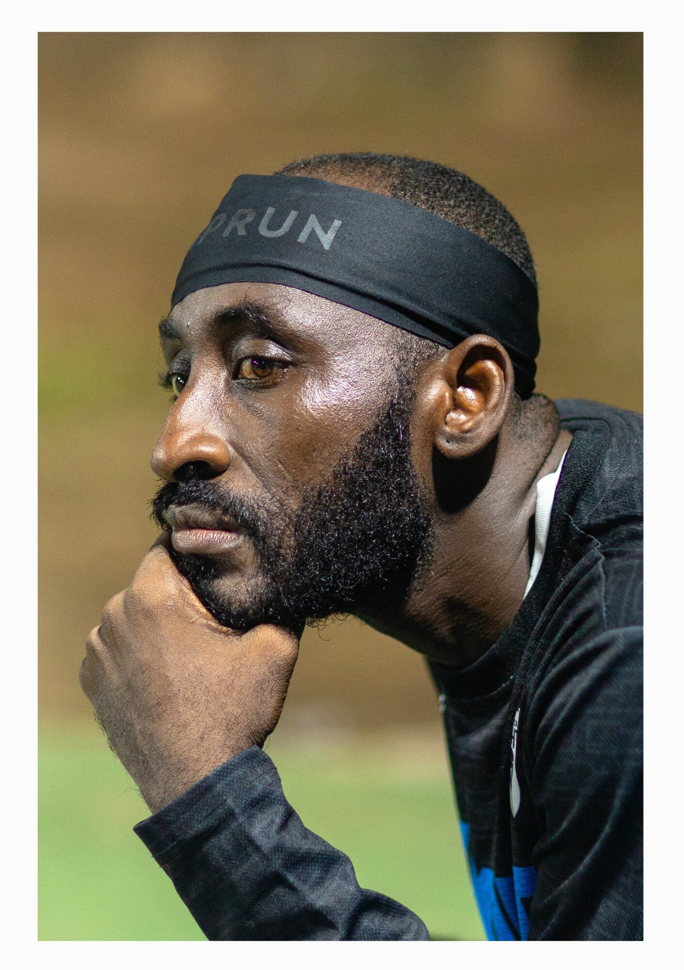Man with a headband resting his chin on his hand, looking thoughtful outdoors.