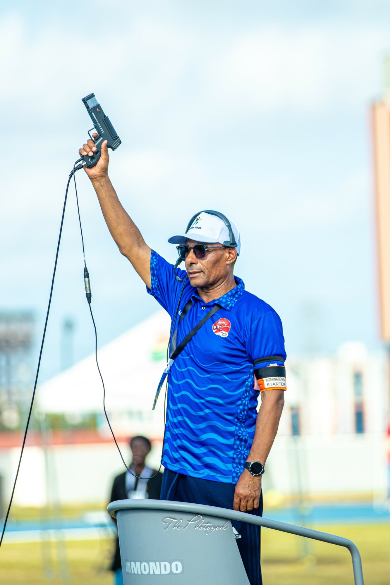 Person in blue shirt and cap holding a device in the air outdoors, with a cityscape background.