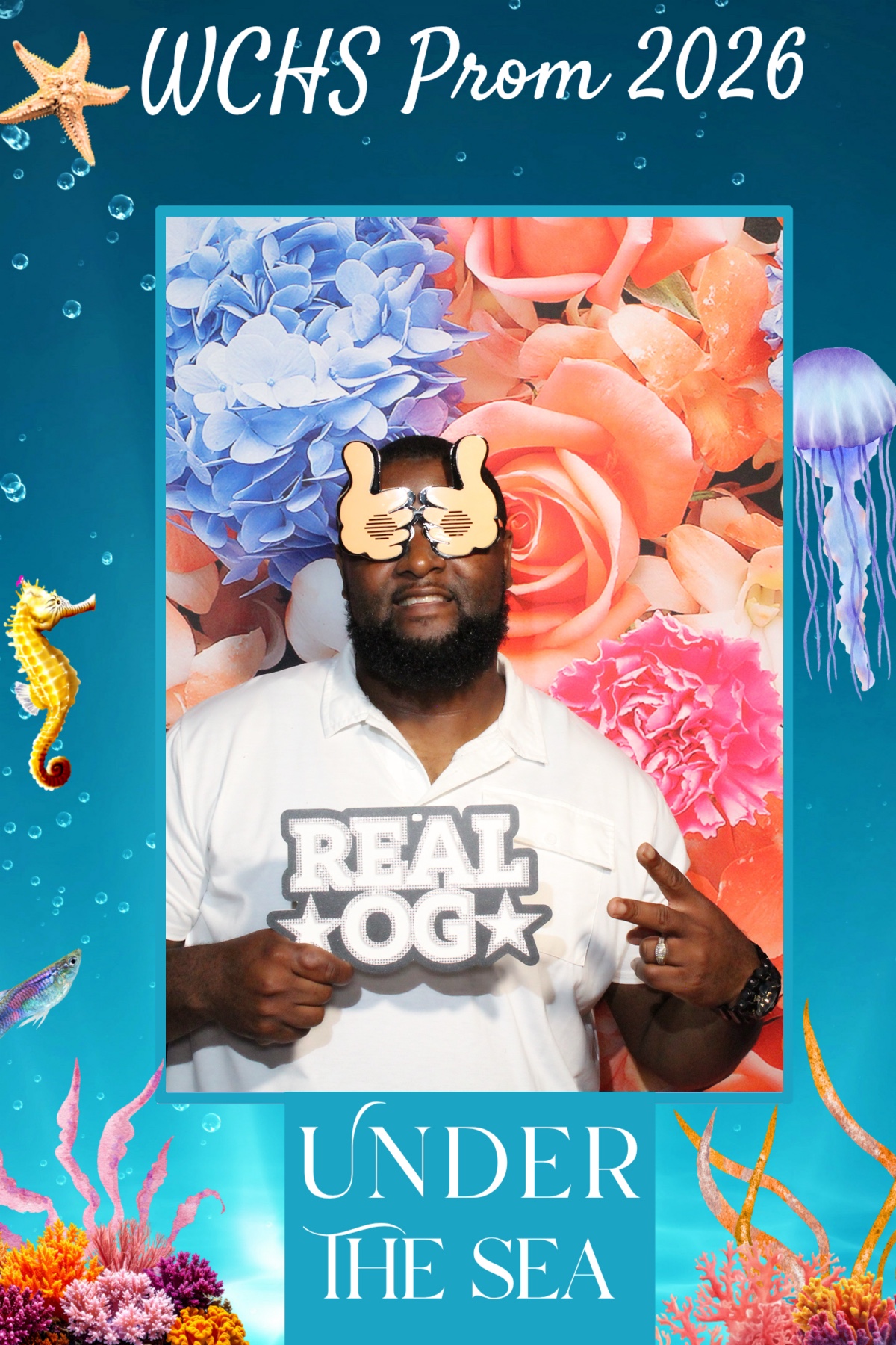 Person holding a sign that says 'REAL OG' with underwater-themed decorations and a floral background.