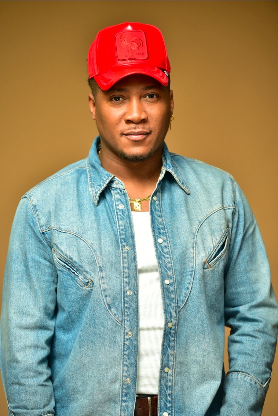 Man wearing a red cap and denim jacket, standing against a plain background.