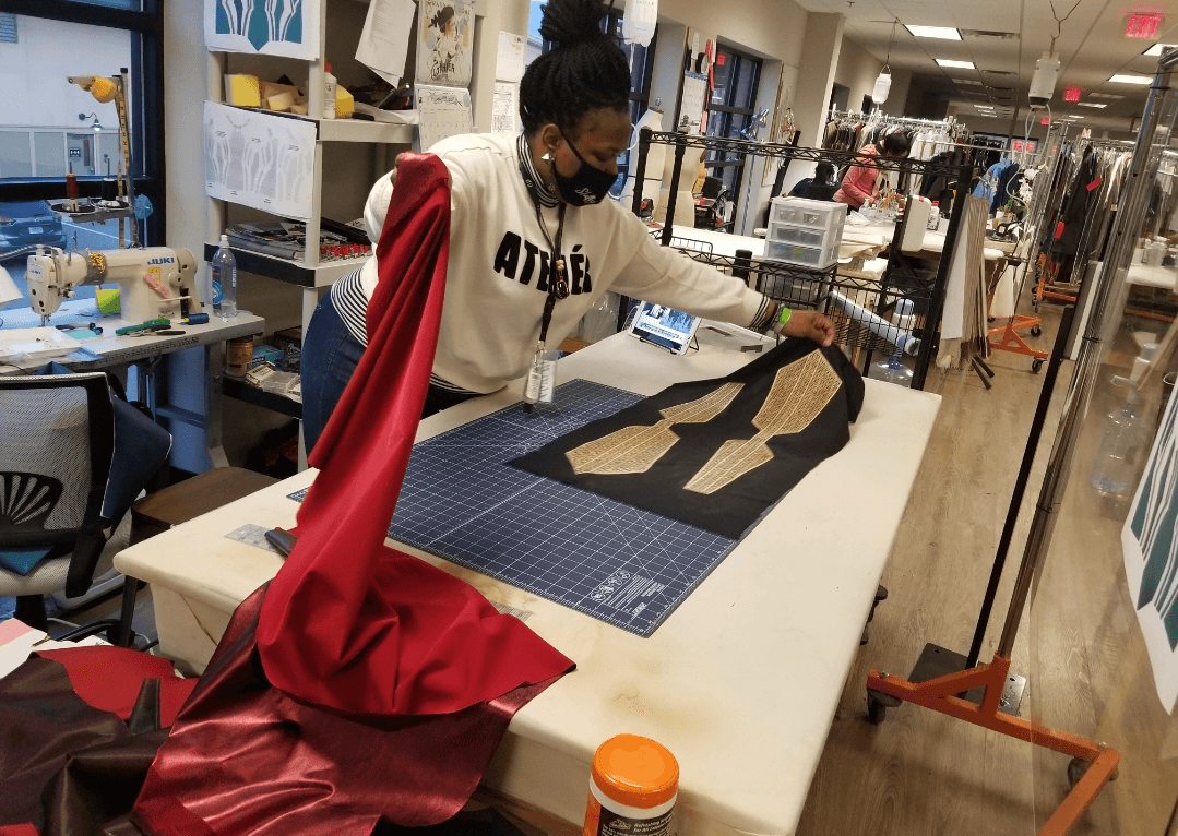 Person working on fabric pattern in a sewing or design studio, surrounded by tools and materials.