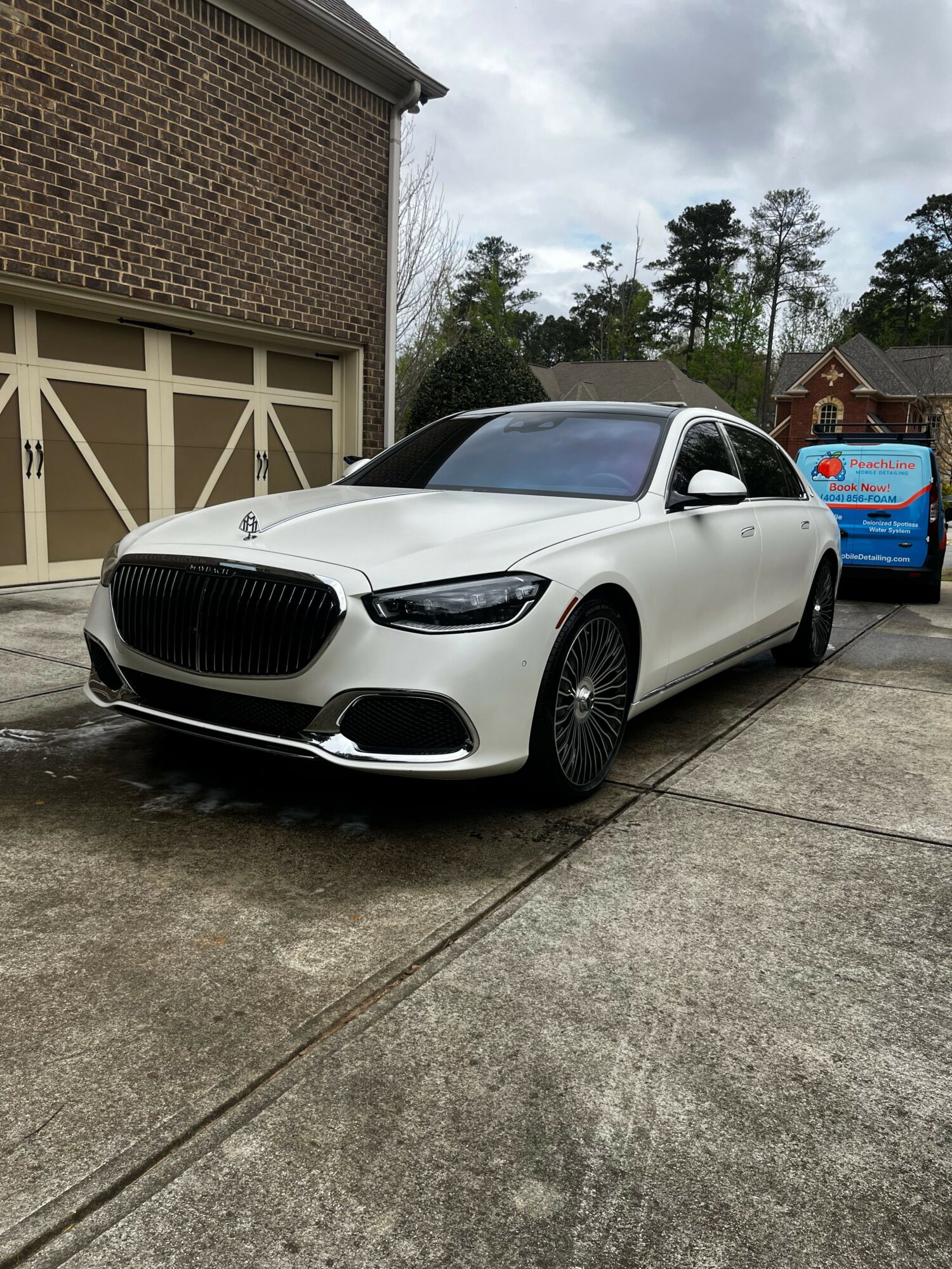 White car parked on driveway with trees and house in background.