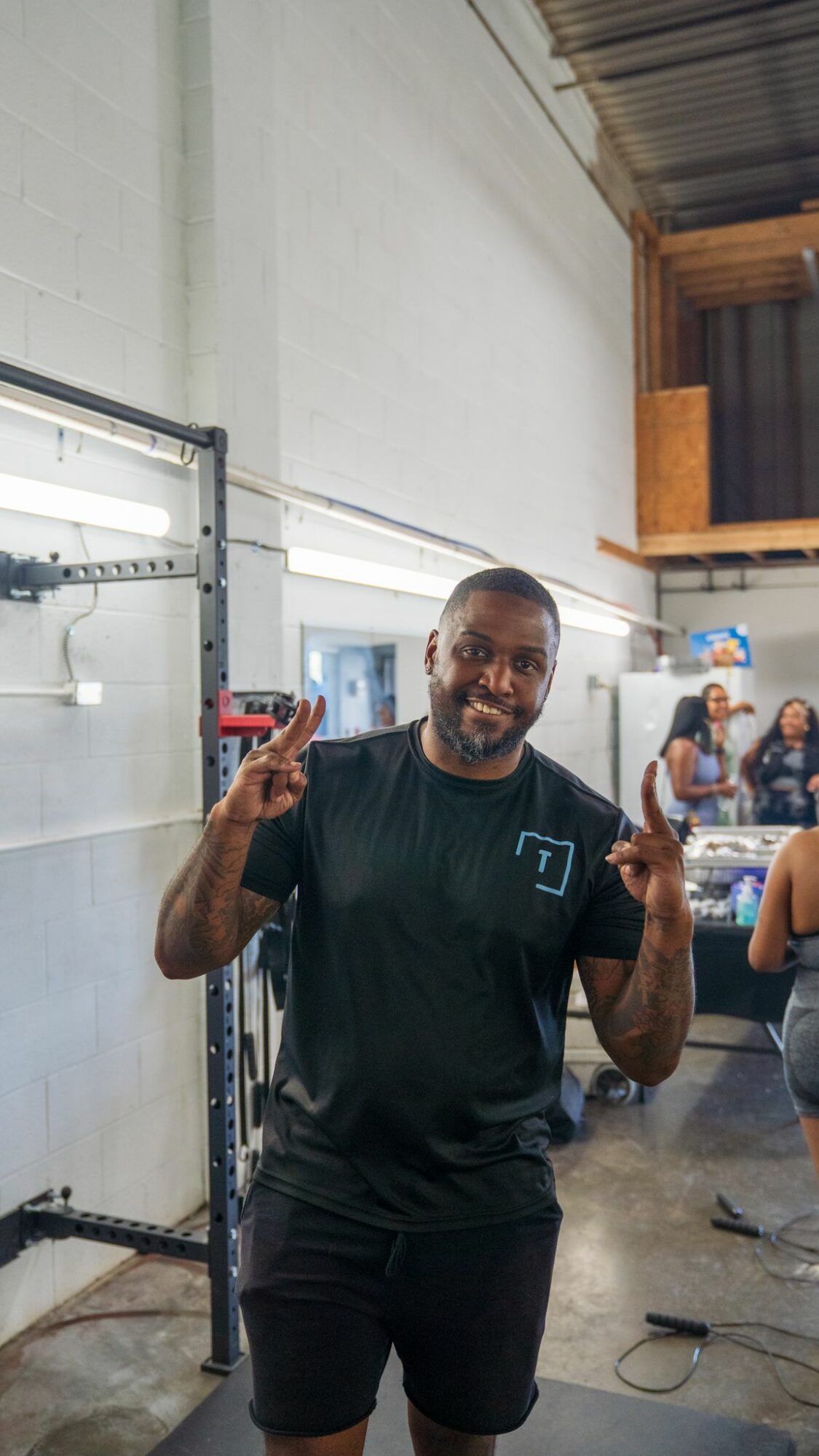 Man smiling and holding a phone in a warehouse or industrial space, with people in the background.