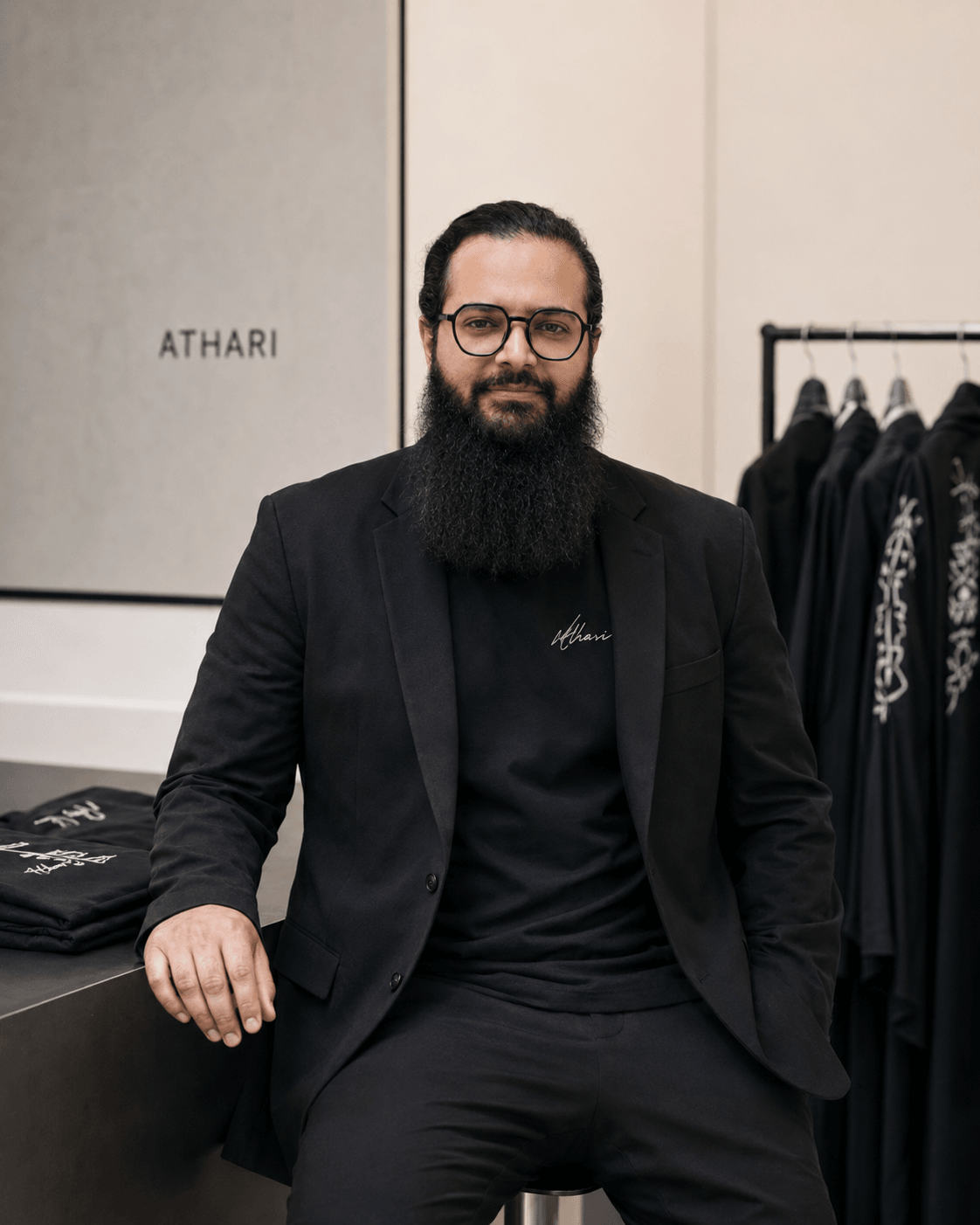 Man with glasses and a beard wearing a black blazer and t-shirt, standing in a clothing store.