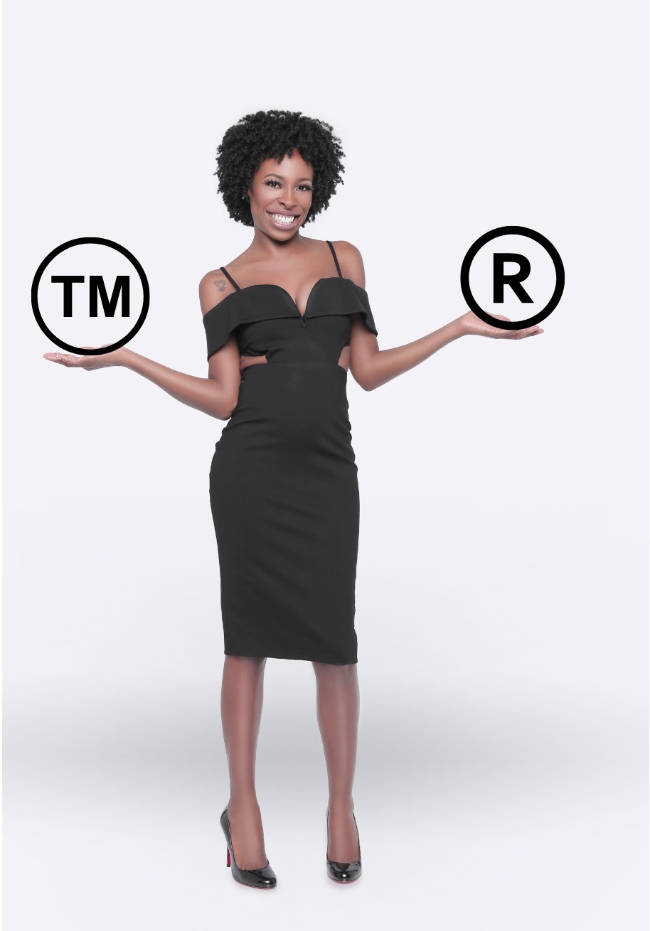 Woman in black dress holding TM and R symbols, smiling, standing against a white background.