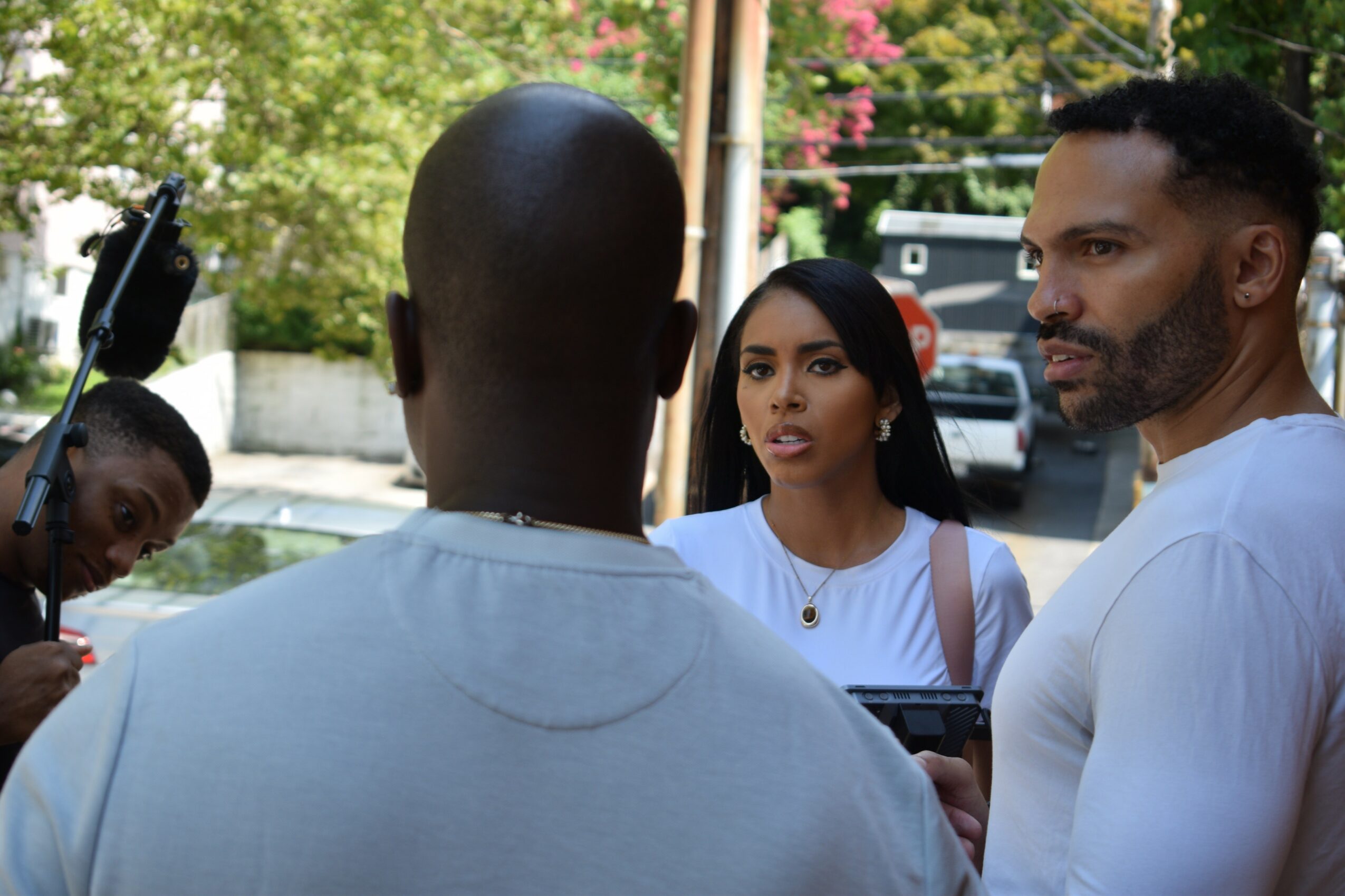 Group of four people outdoors, two women and two men, engaged in conversation, with trees and a street in the background.