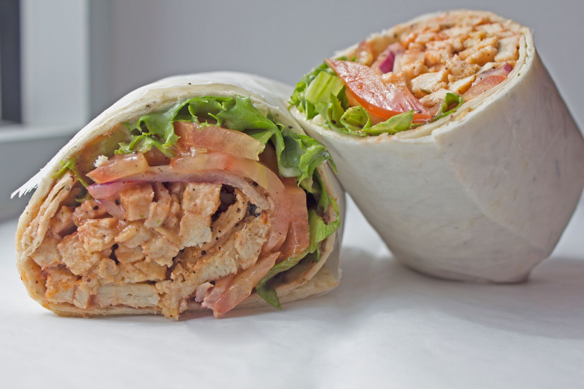 Two burritos with lettuce, meat, and vegetables on a white surface, one cut in half showing filling.