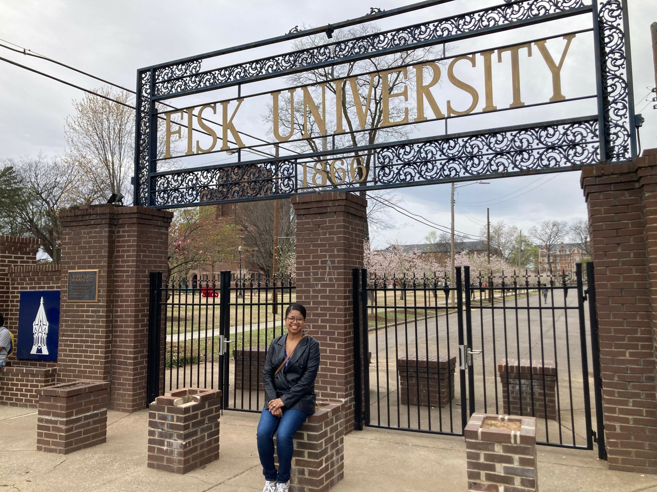 Person standing in front of a university gate with a sign reading 'FISK UNIVERSITY'.