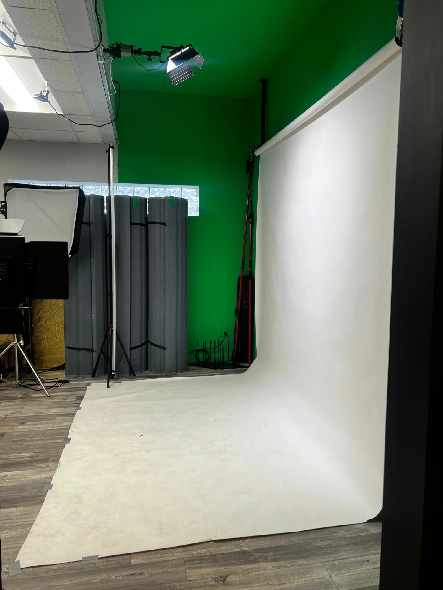 Photo of a photo studio with a green screen, a white backdrop, and studio equipment, viewed from an angle.