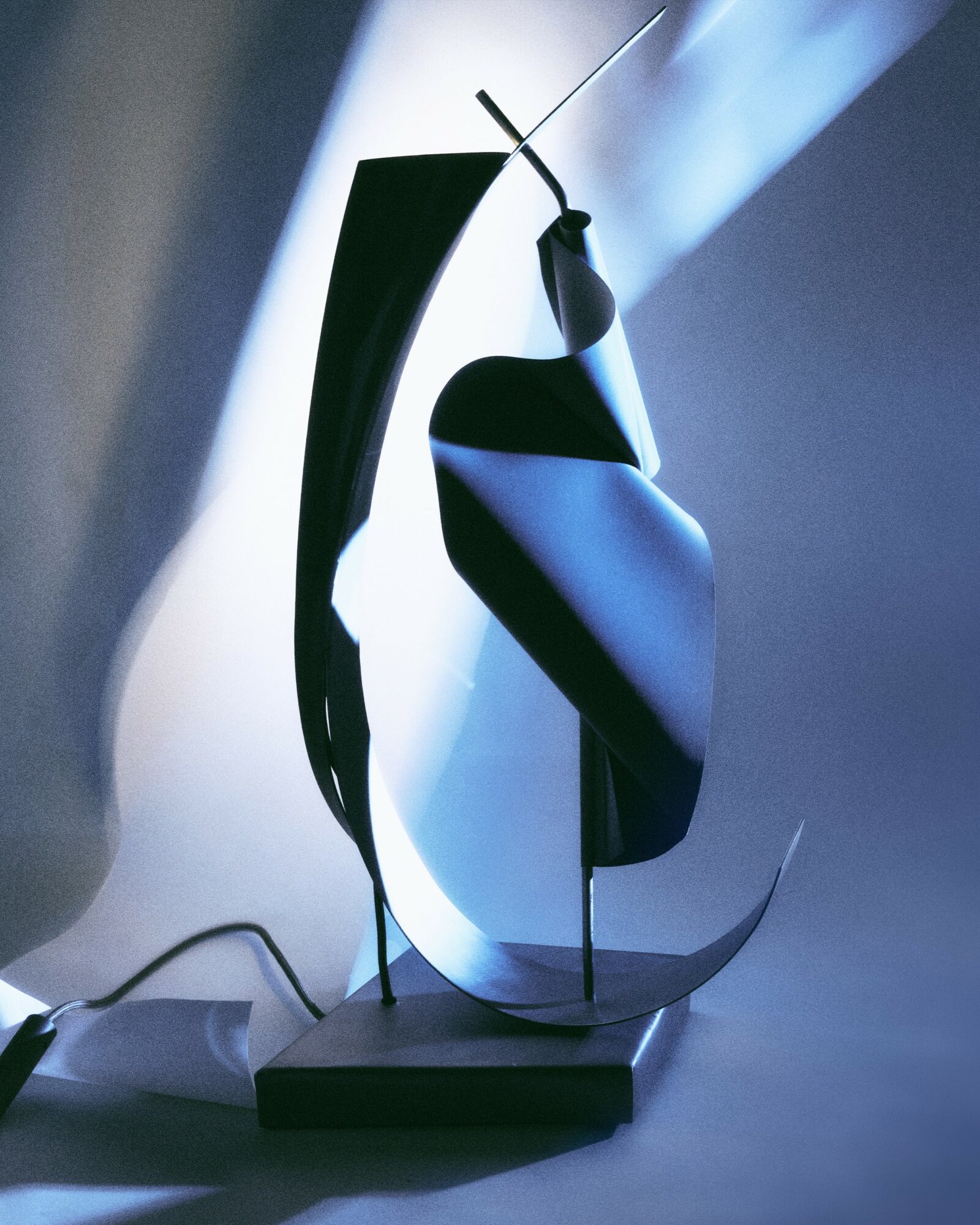Abstract sculpture with curved black and white elements on a base, illuminated by soft light.