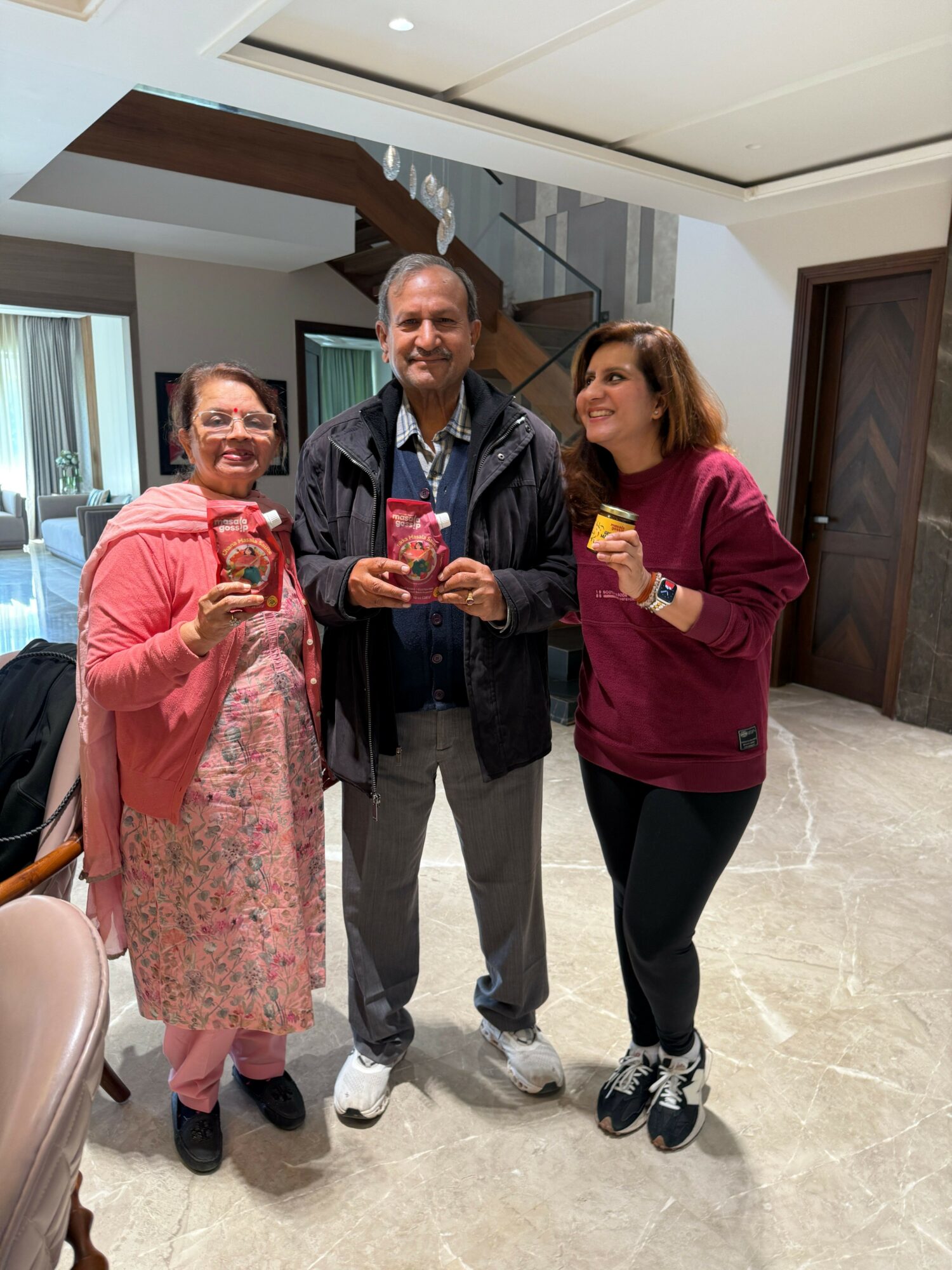 Three women standing indoors, one holding a small object, all smiling and looking at the camera.
