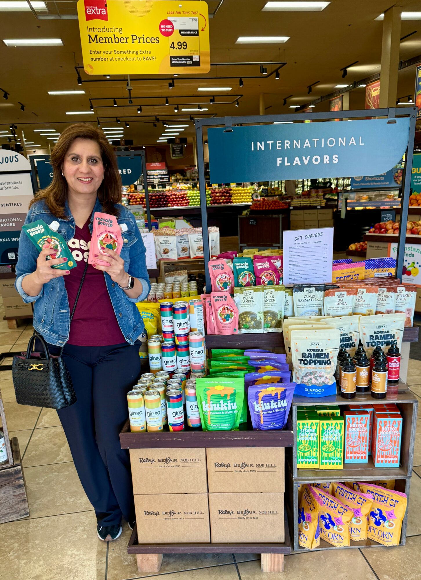Woman standing next to a display of health and wellness products in a store, holding two items, smiling.