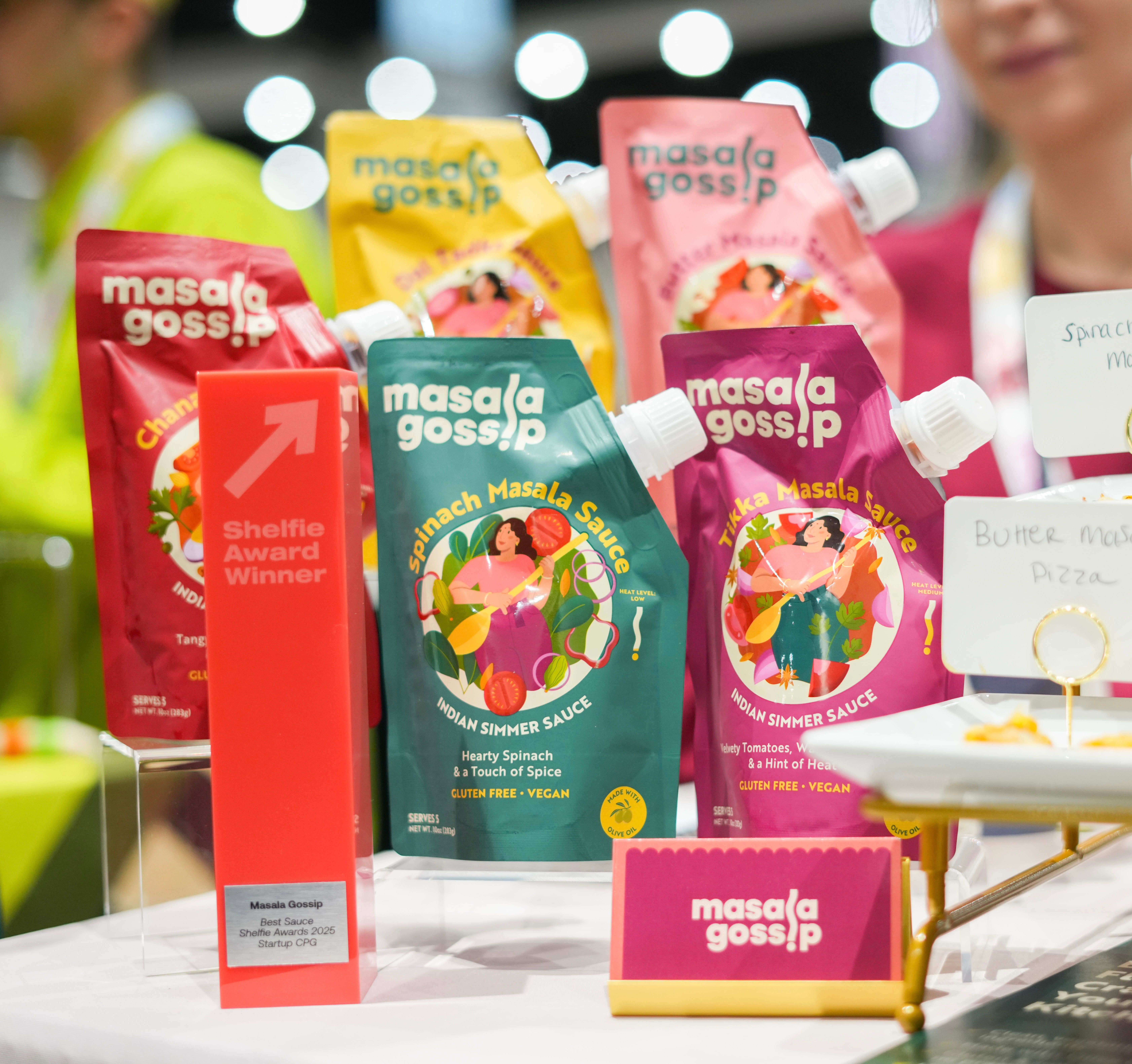 Display of various colorful sauce packets on a table, with a pink sign and a red award trophy in the foreground.