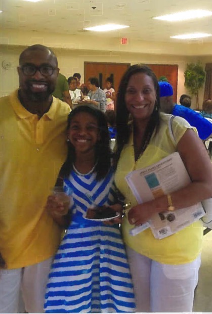Three people smiling indoors, holding papers and a phone, with other guests in the background.