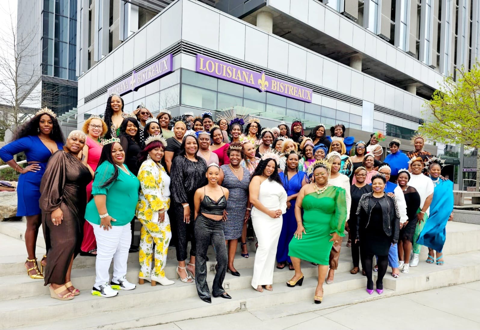 Group of diverse women and men standing outside a building with a sign reading Louisiana. They are smiling and posing for a photo.