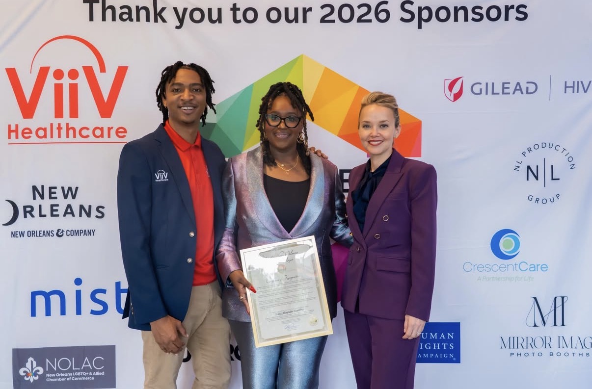 Three people standing together holding a certificate at an event, with a colorful backdrop and sponsor logos.