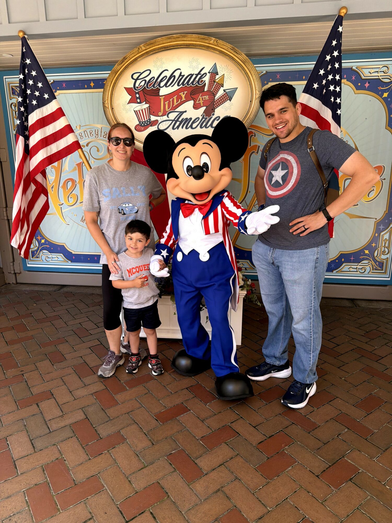 Family with Mickey Mouse character, two children, and two adults, standing in front of patriotic decorations and a sign celebrating July 4th.
