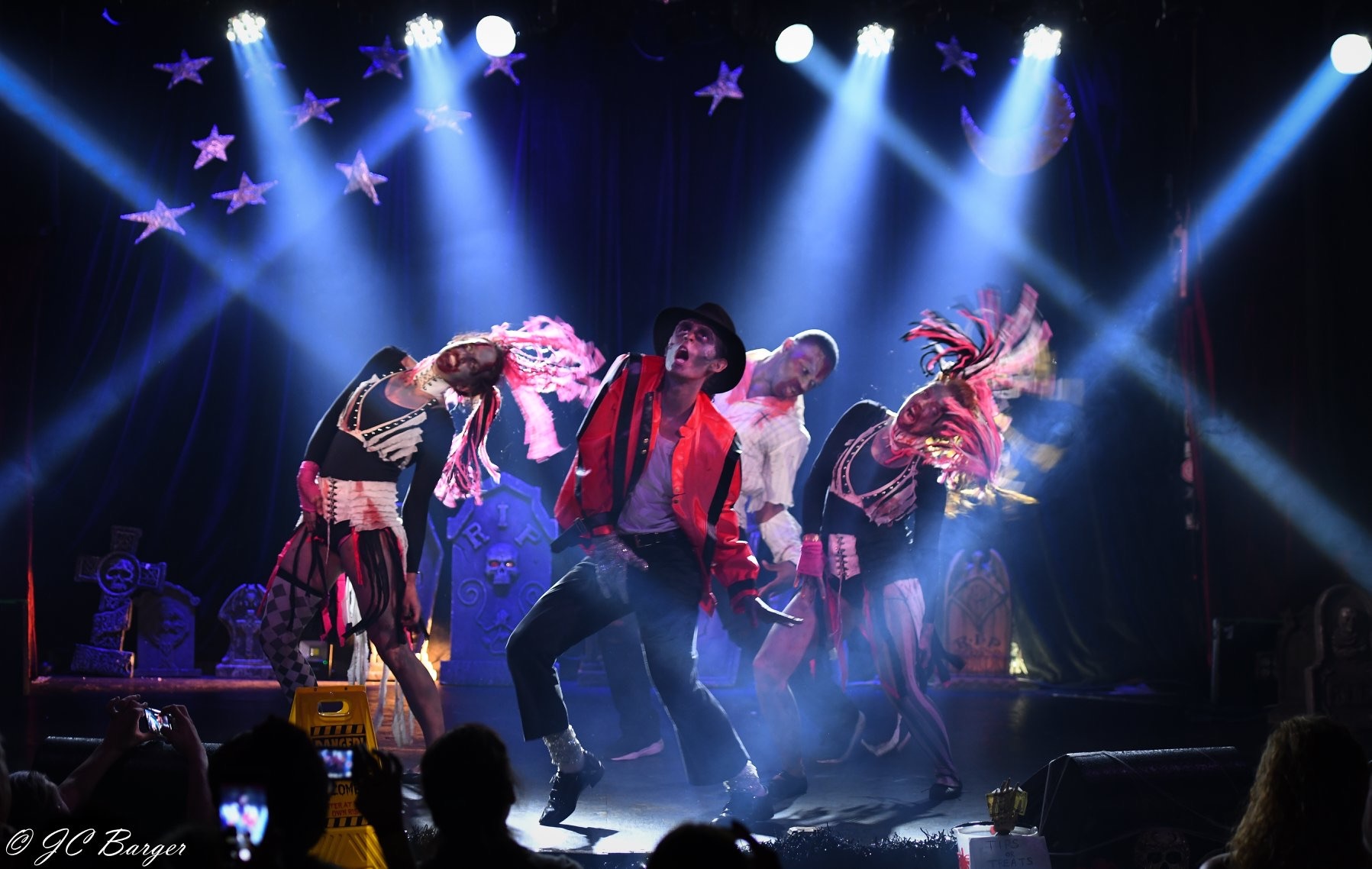 Group of performers dancing on stage with colorful lights and star decorations in the background.