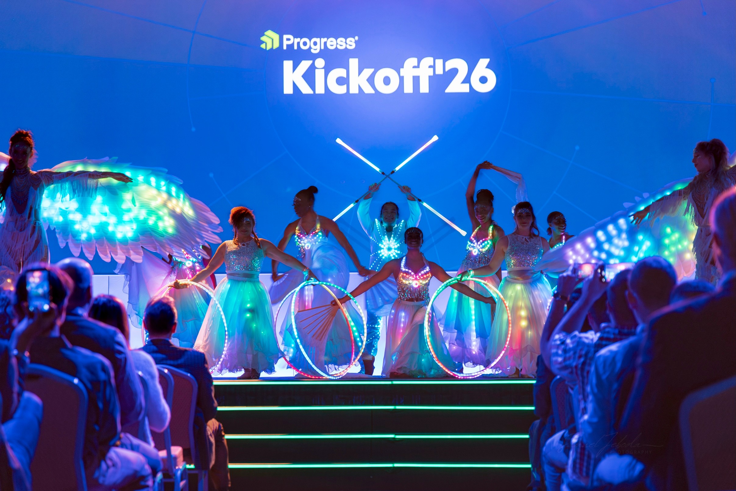 Stage with dancers holding hoops, audience watching, and a screen displaying 'Progress Kickoff 26' in the background.