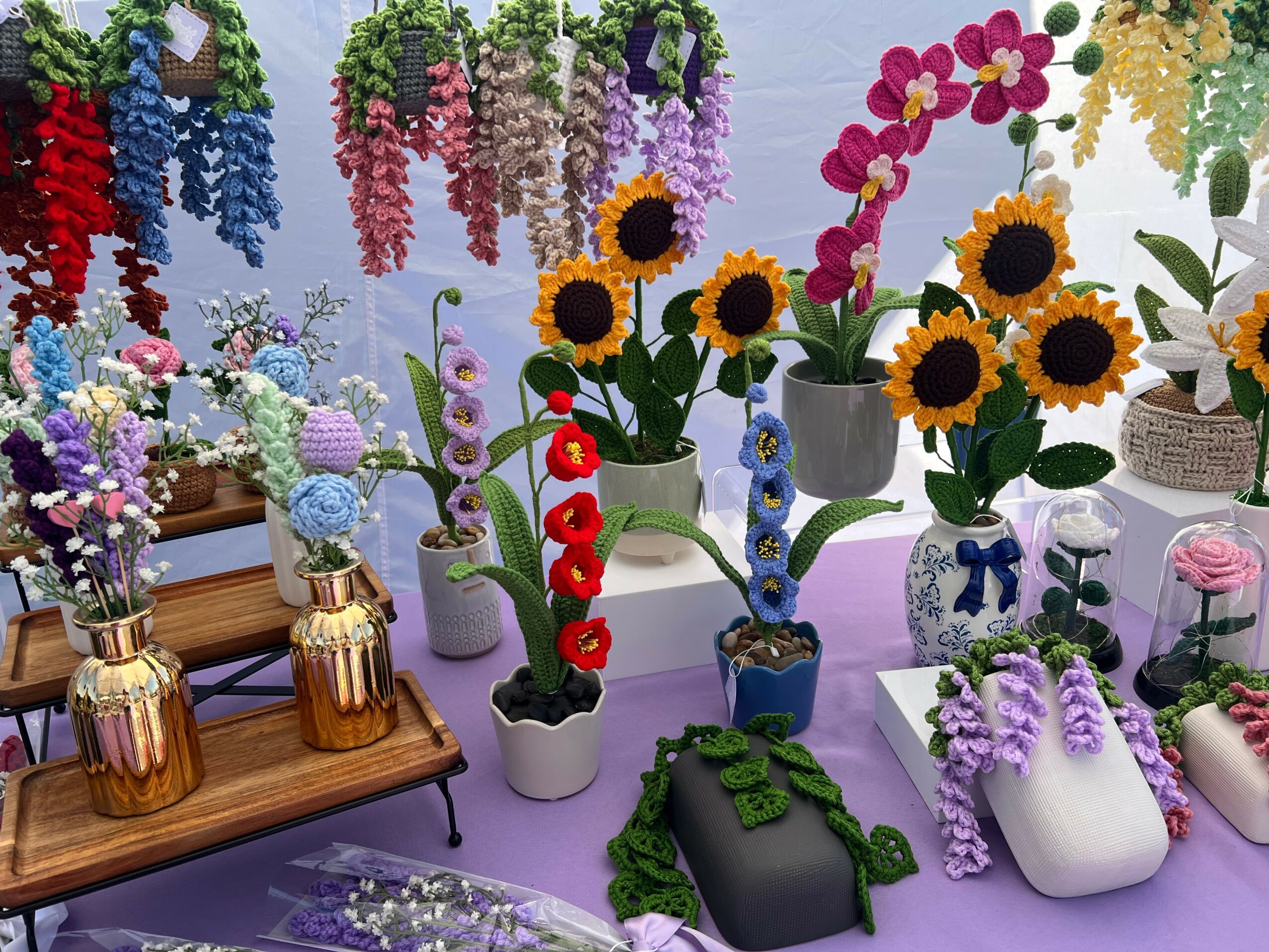 Display of colorful flowers in vases and pots, including sunflowers, orchids, and lavender, arranged on tables and shelves.