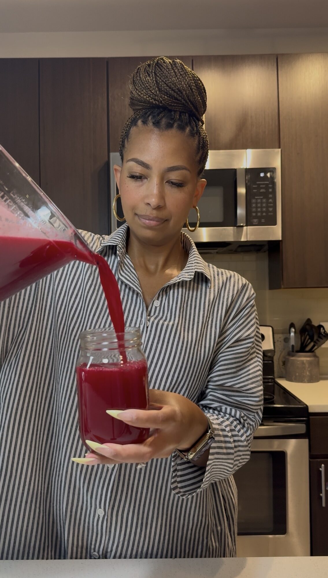 Woman pouring a red beverage into a glass in a kitchen, wearing a striped shirt, with a microwave in the background.