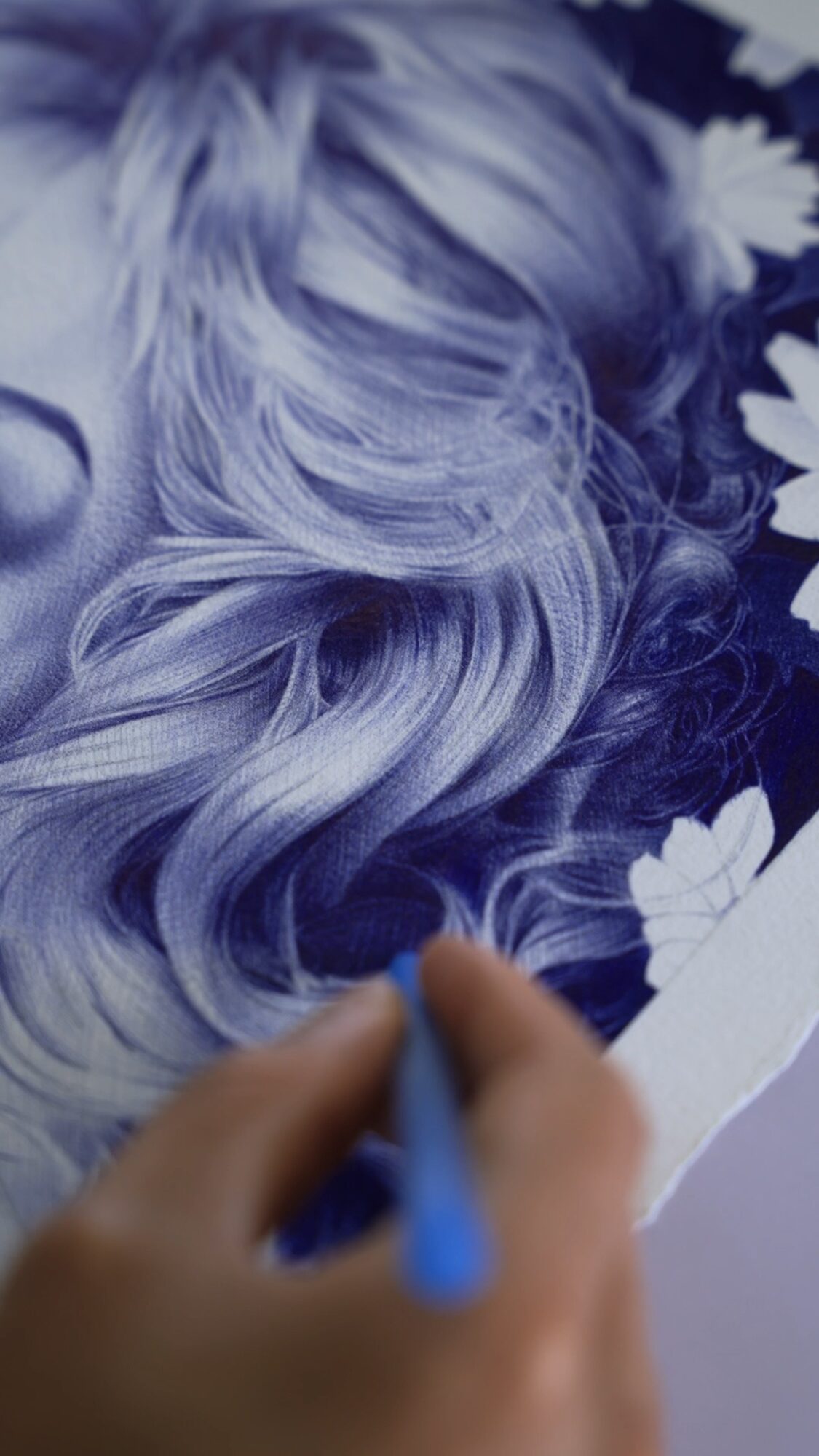 Close-up of a hand drawing on a photo of a person with long, wavy hair surrounded by flowers.