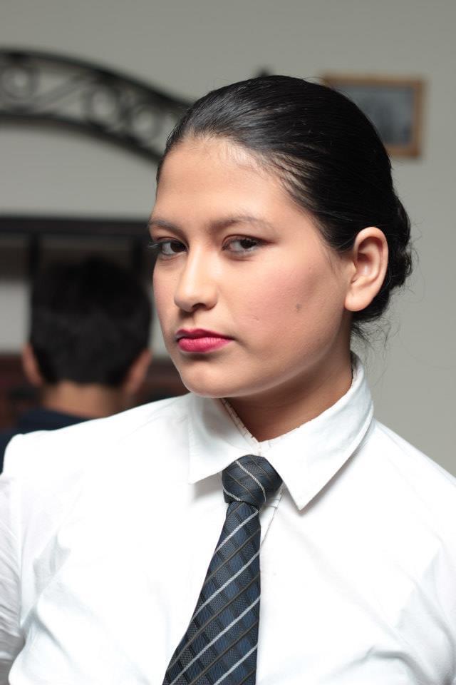 Young woman with dark hair in a bun, wearing a white shirt and striped tie, looking at the camera.