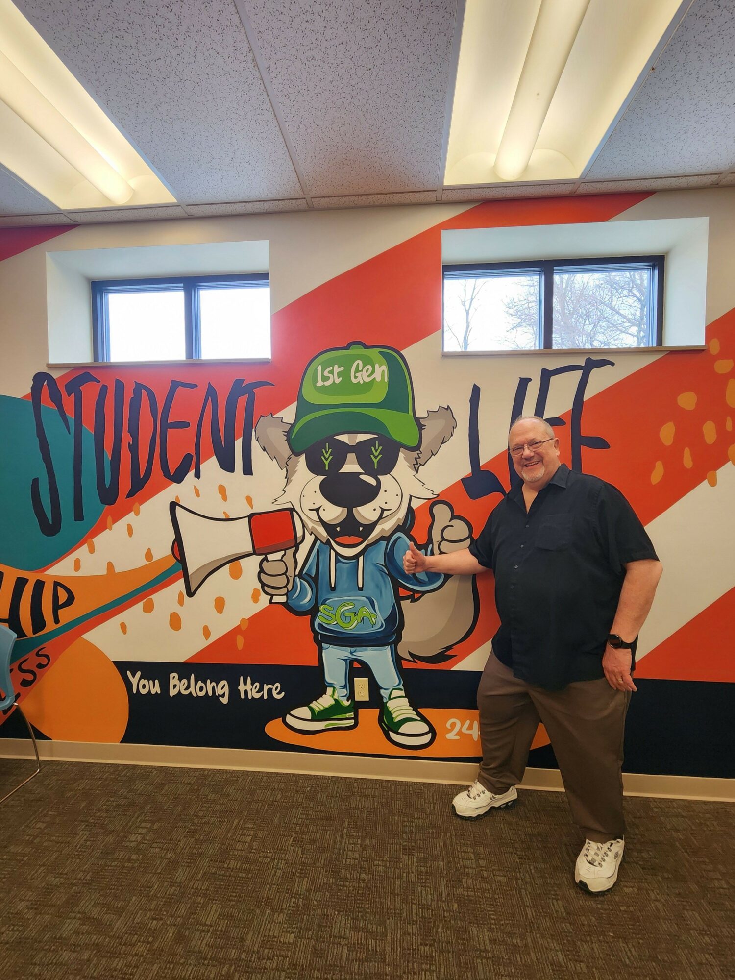 Person standing next to a colorful superhero-themed display with a cartoon character and text, indoors.