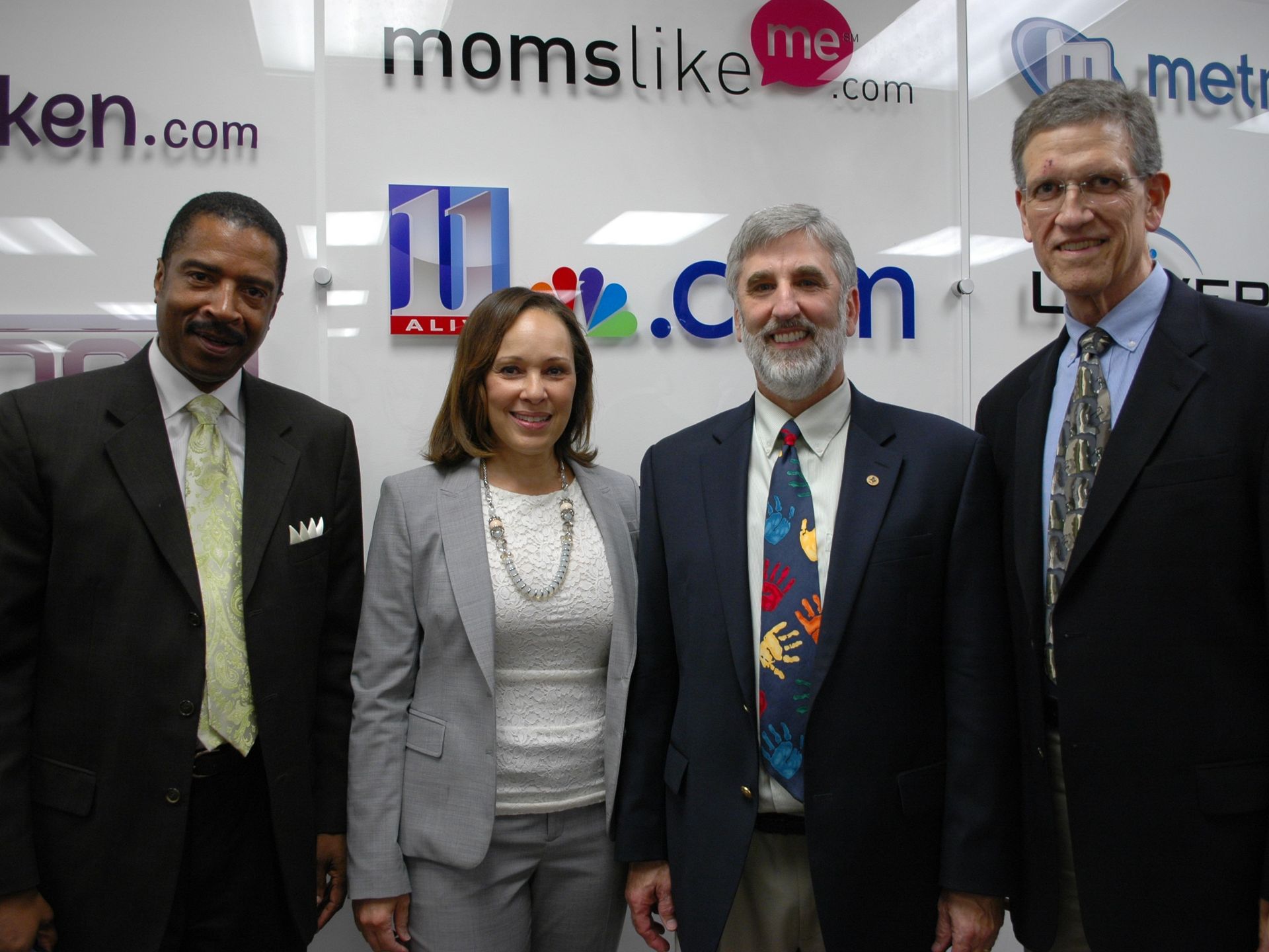 Four people standing in front of a backdrop with logos and text, smiling for the photo.