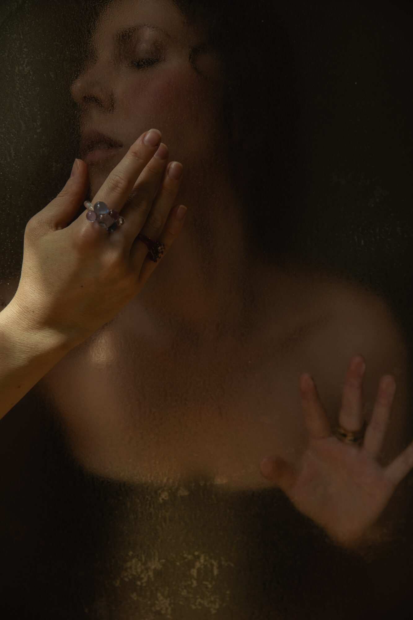 Person with hand near face, wearing rings, partially visible face, dark background