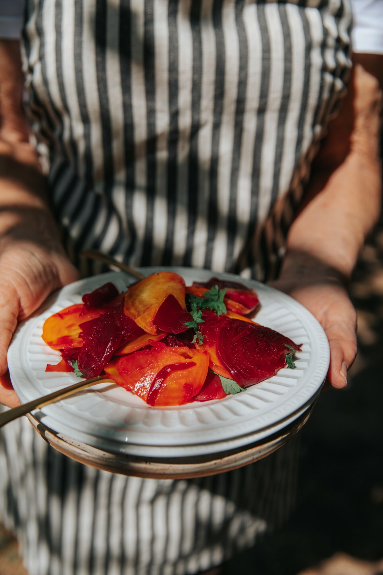 Person holding a white plate with colorful fruit slices and garnishes, wearing a striped apron.