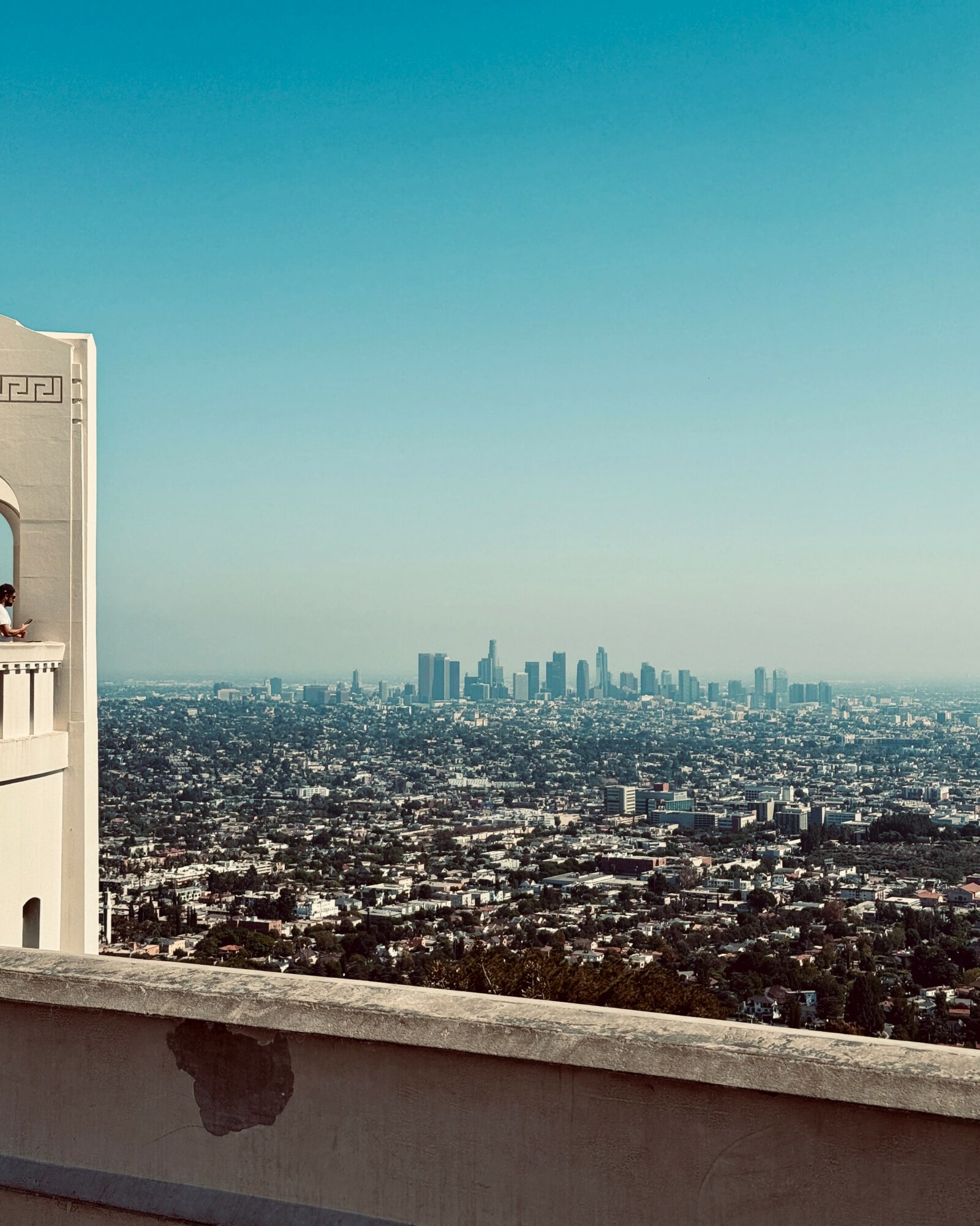 City skyline with tall buildings in the distance, viewed from a rooftop with a ledge, under a clear blue sky.