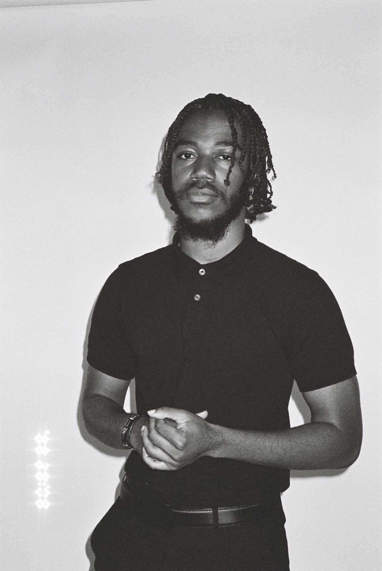 Person with braided hair wearing a dark shirt and pants, standing with arms crossed, facing camera.