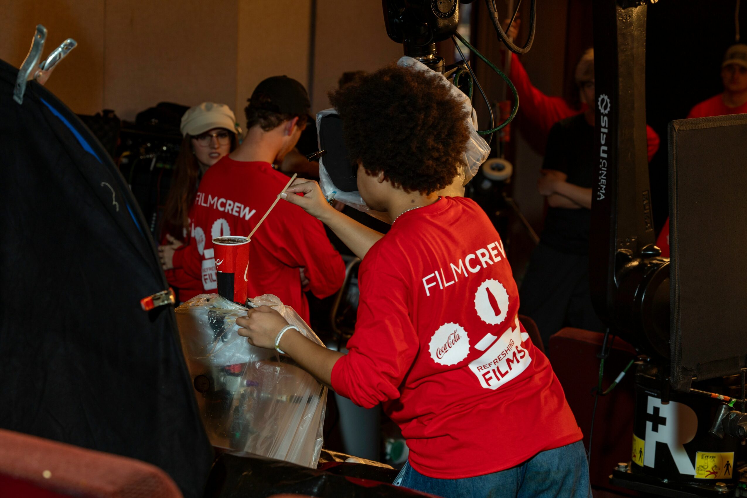 Group of people wearing red shirts working with equipment in a room, some with curly hair, focused on tasks.