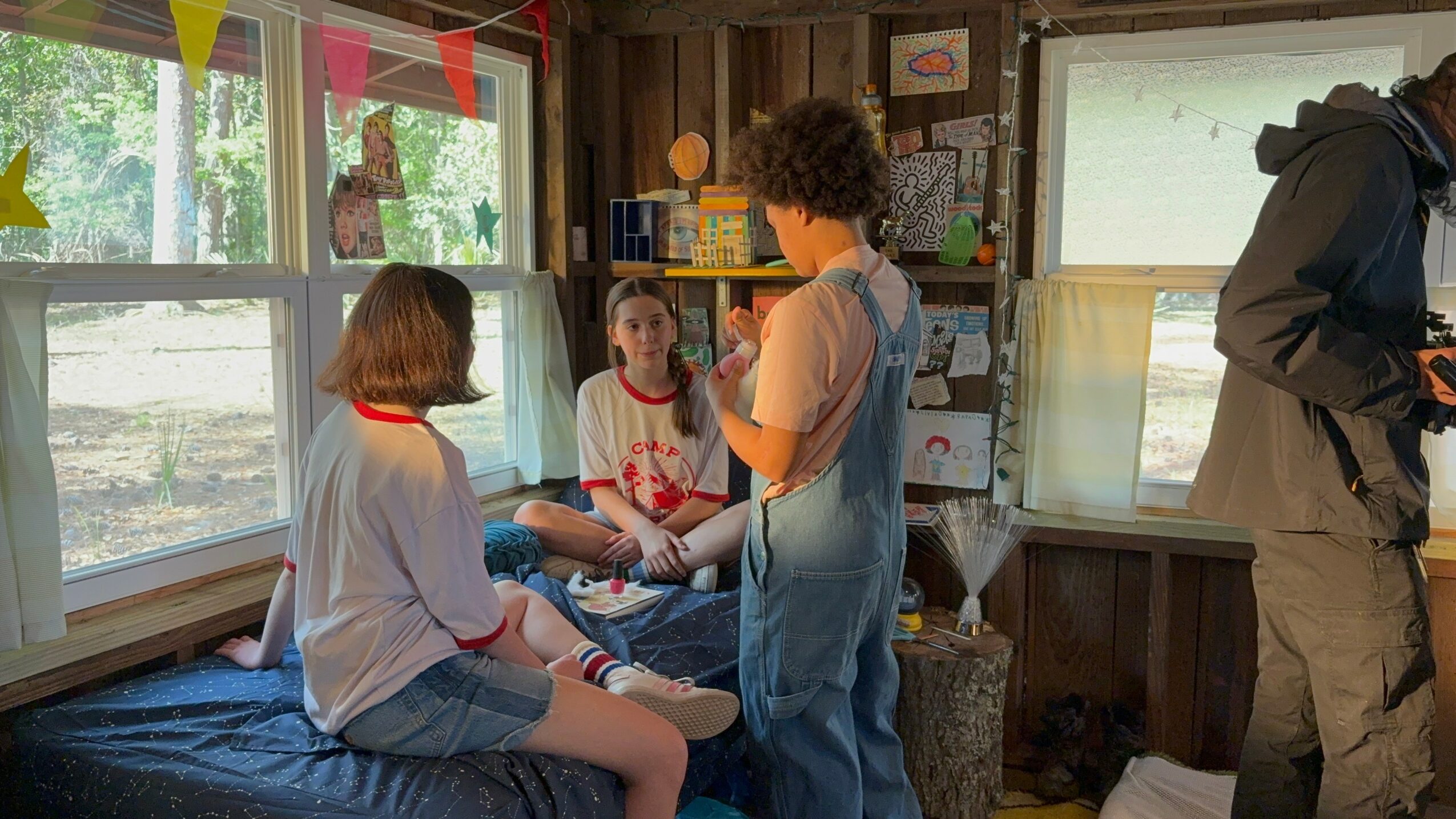 Three children in a cozy room with large windows, sitting and standing, engaging in conversation or activity.