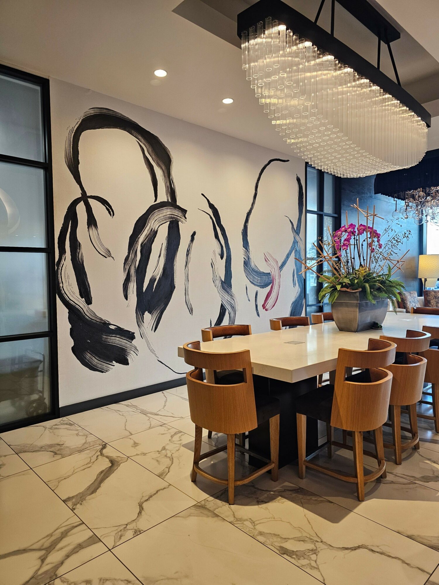 Interior with a large abstract painting, a dining table with chairs, and a window with plants.