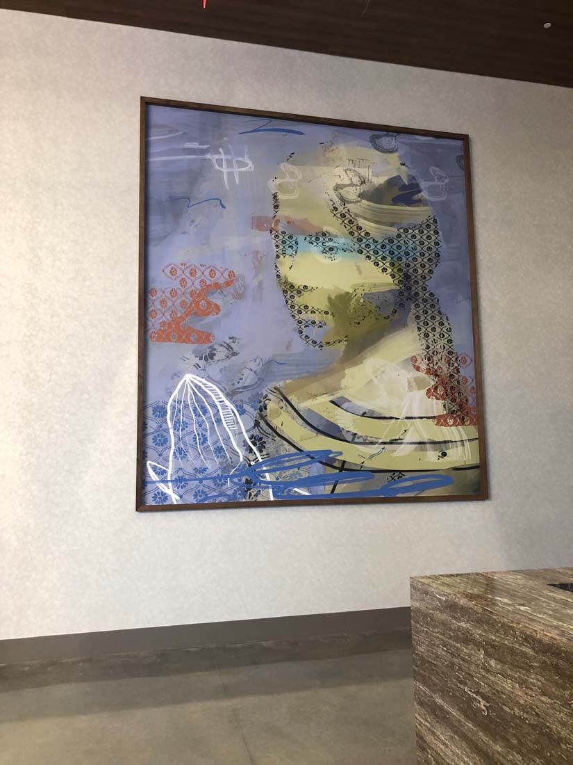Abstract painting of a human face with various colors and patterns, framed on a wall, with a stone surface in foreground.
