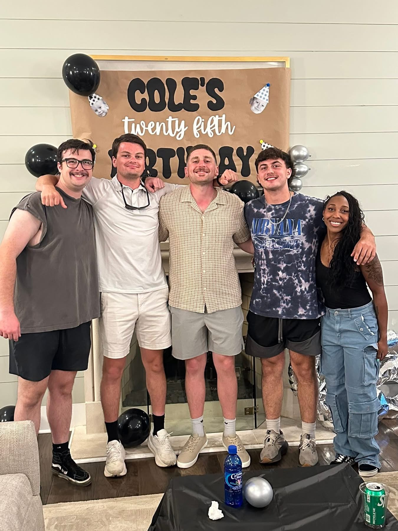 Five people standing together in front of a decorated backdrop, smiling, with balloons and a sign reading 'Cole's twenty fifth birthday' behind them.